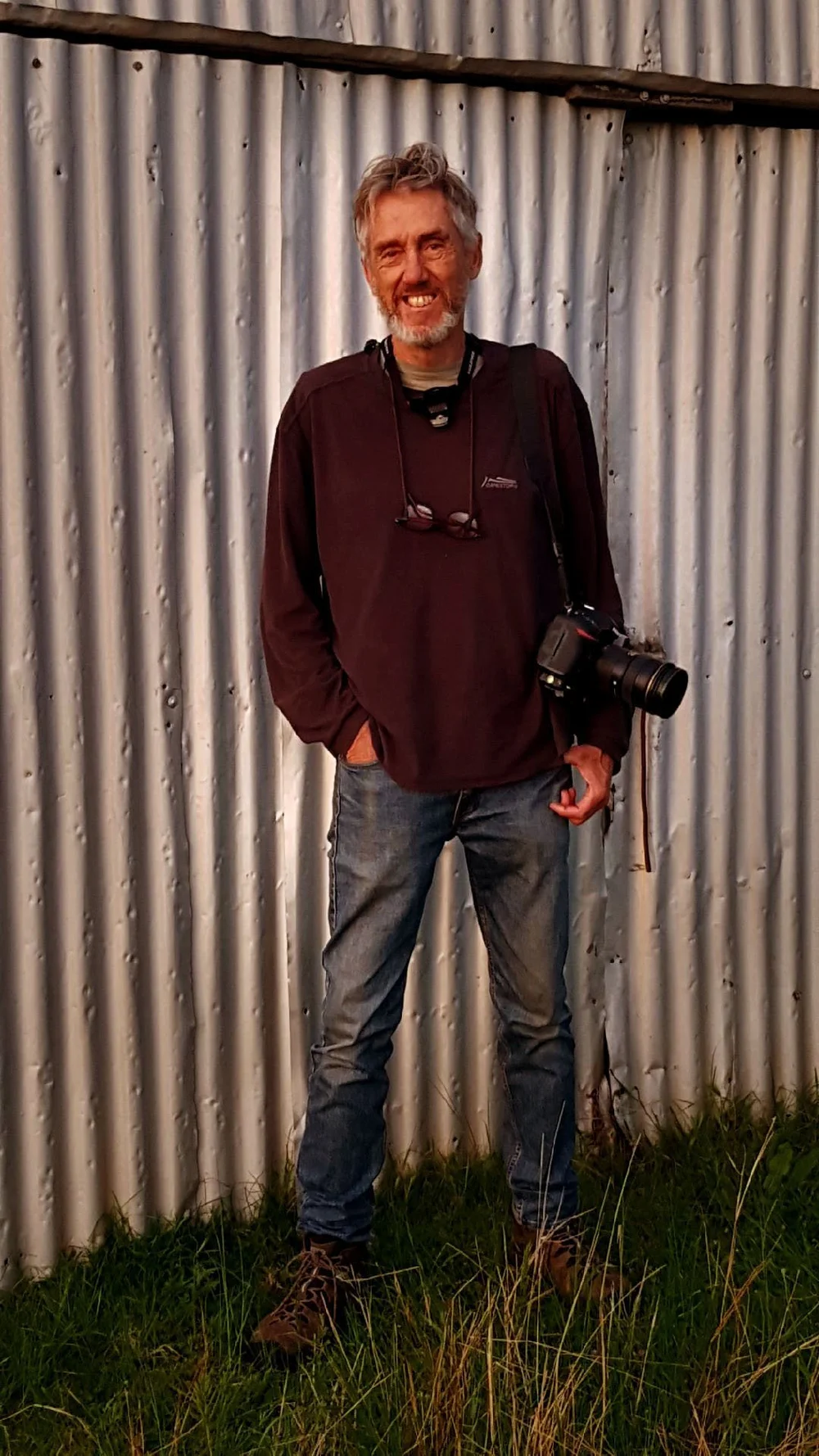 Peter Solness standing with his camera against a corrugated iron wall